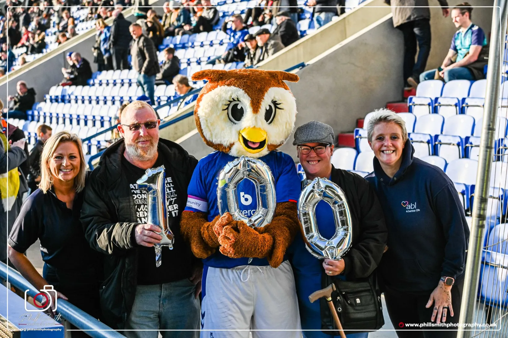 Ex-smokers and Your Health Oldham members at Oldham Athletic Stadium with 'Chaddy the Owl' and coaches Lorraine and Kidella. Holding 100 balloons to celebrate 100 days quit.